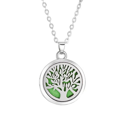Collar difusor de aromaterapia en acero inoxidable con diseño de árbol y fondo verde, ideal para aceites esenciales.